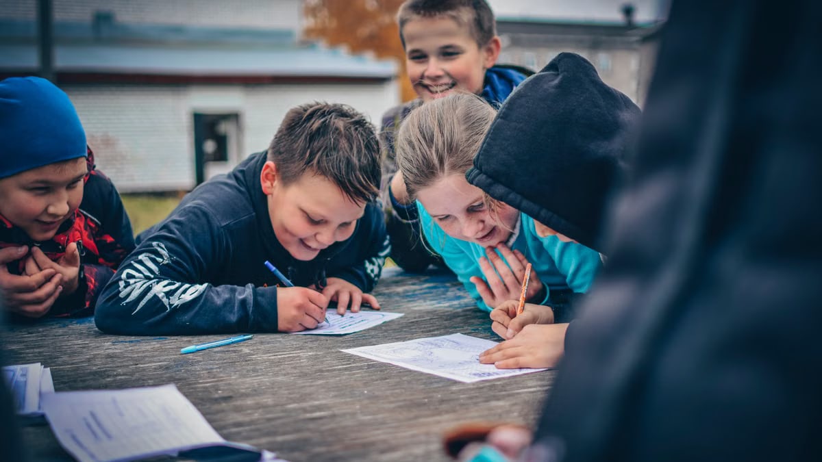 Happy children drawing together outdoors on a wooden table, fostering creativity and teamwork.